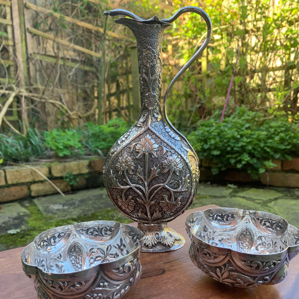 Photo of some Indian silver finger bowls on a wooden surface with a garden in the background